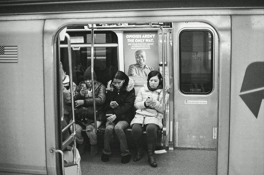 Black and white photo of commuters using smartphones on a subway in New York City.