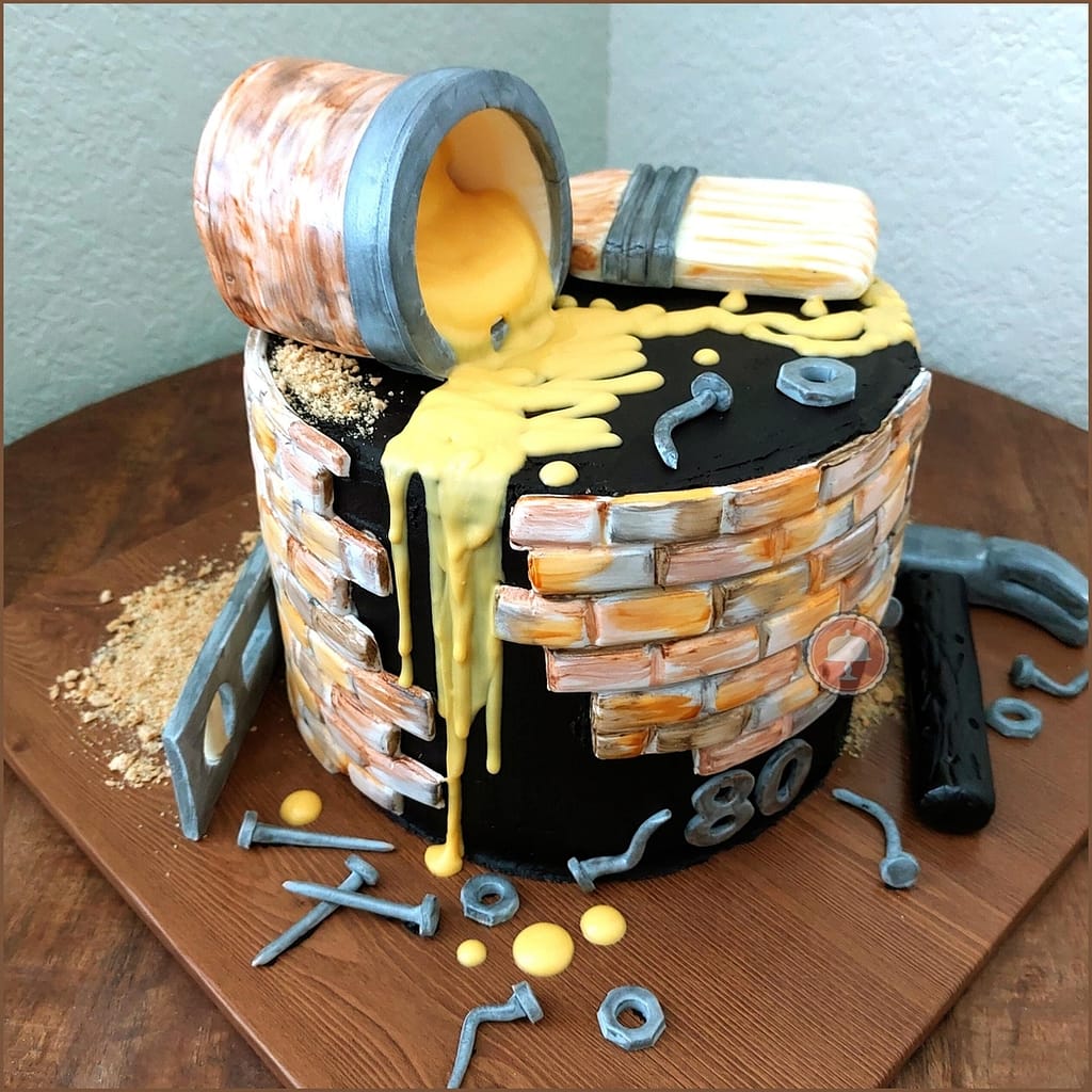 carpenters cake ideas that has a hammer, level, nails around the base of a three tier cake and paint dripping from a spilled can of yellow paint on top