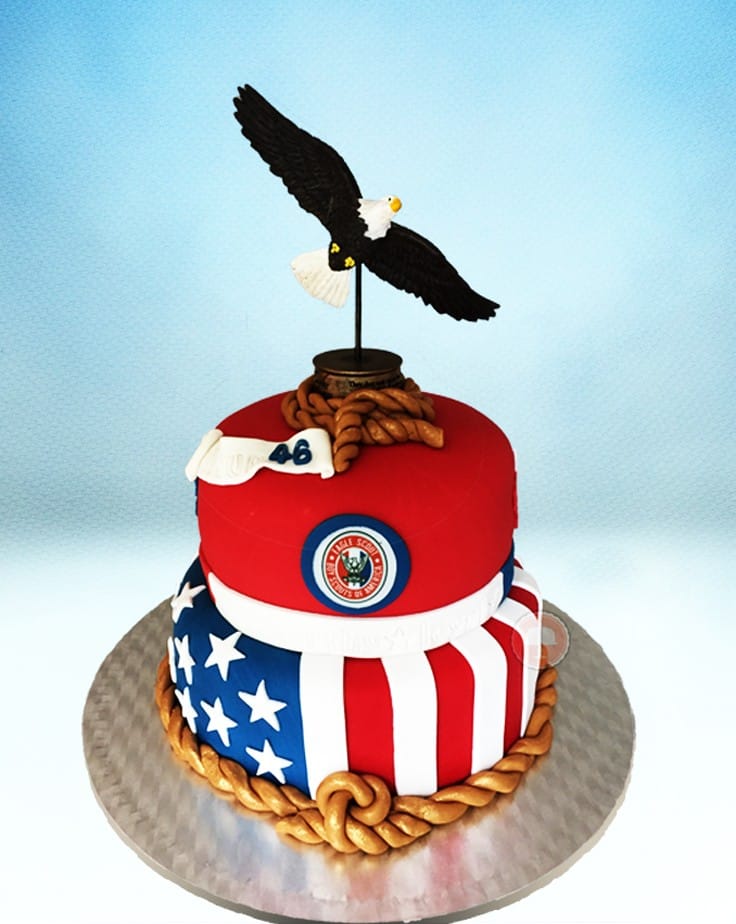 eagle scout cake design with fondant and eagle topper sits a a silver cake board and shows the American Flag and eagle scout logo
