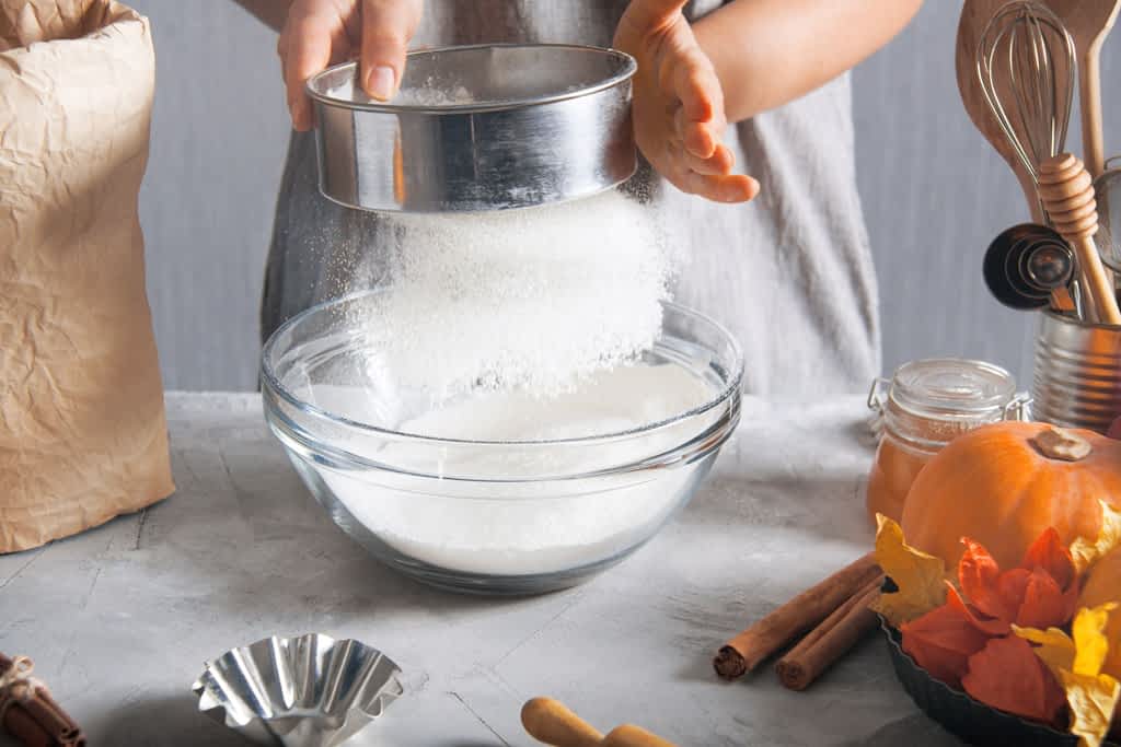 person sifting flour dry ingredients before baking