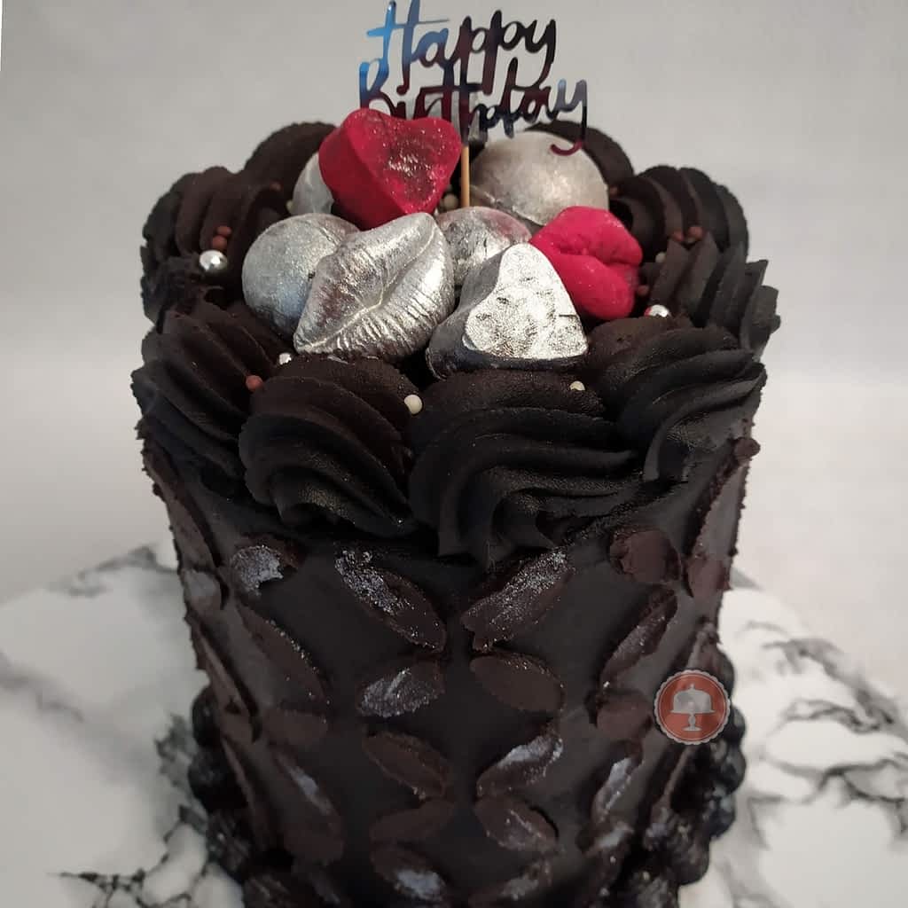 rich dark chocolate birthday cake with decorative piping stencil design topped with hand made chocolates coated in edible luster dust 